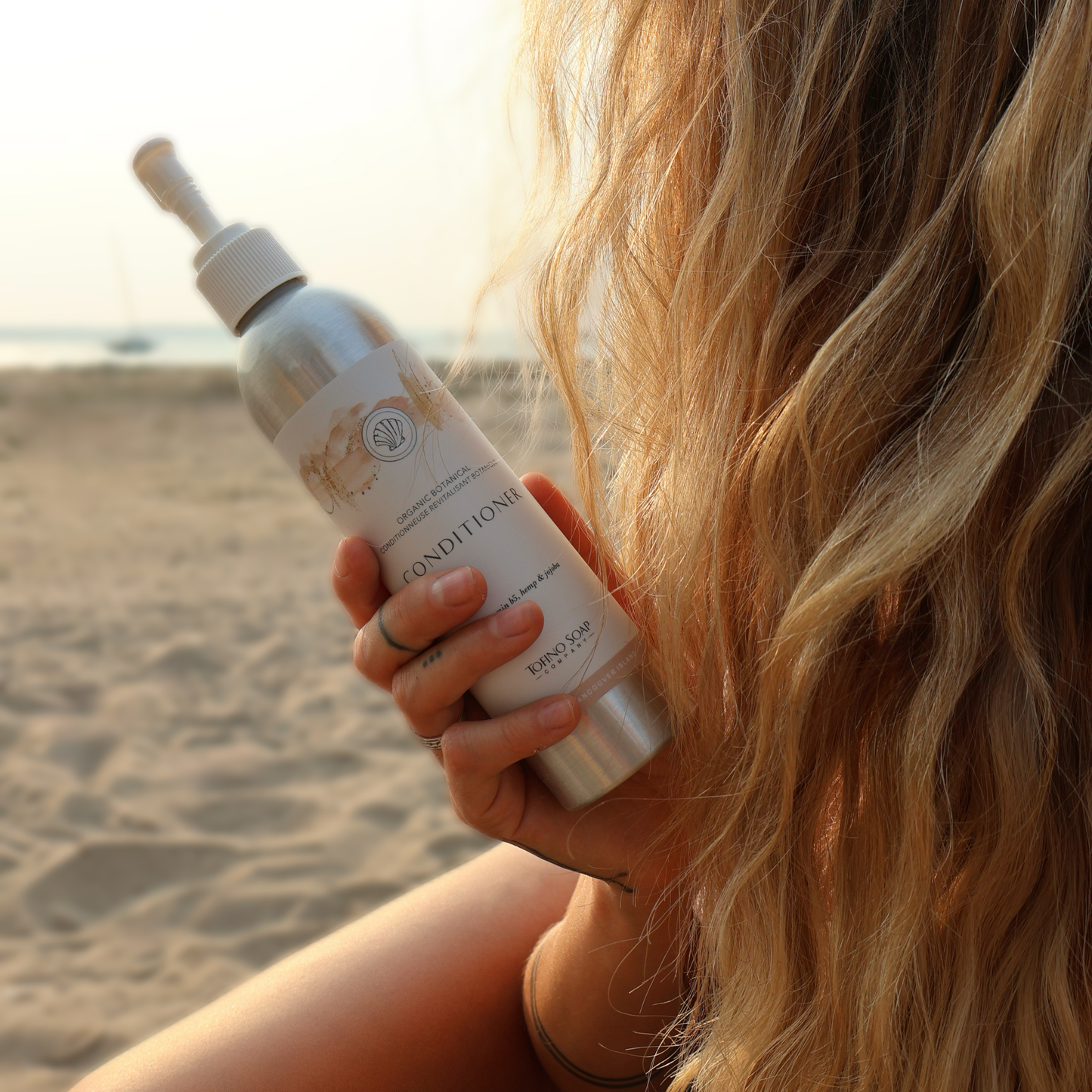 Person holding a bottle of conditioner on a beach