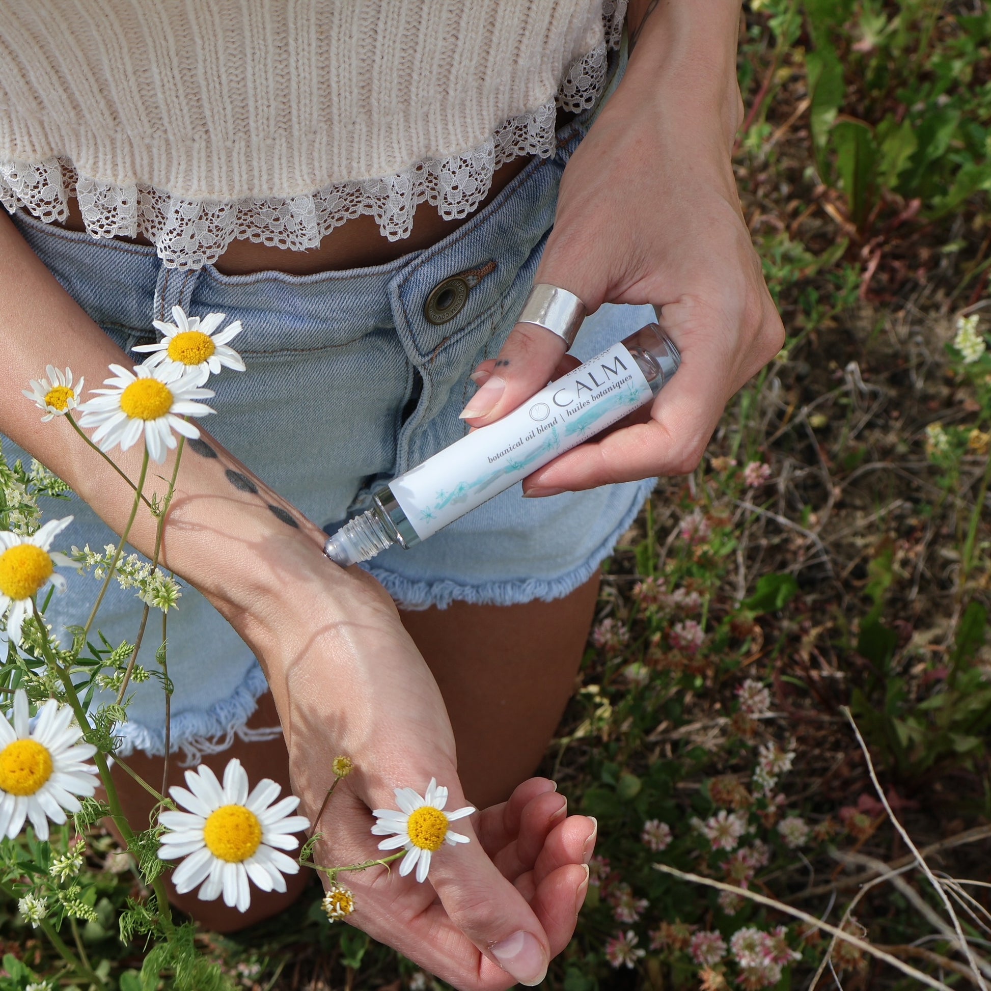 calm roll on being applied to wrists in daisy field