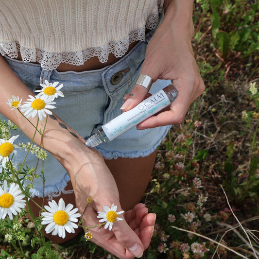 calm roll on being applied to wrists in daisy field