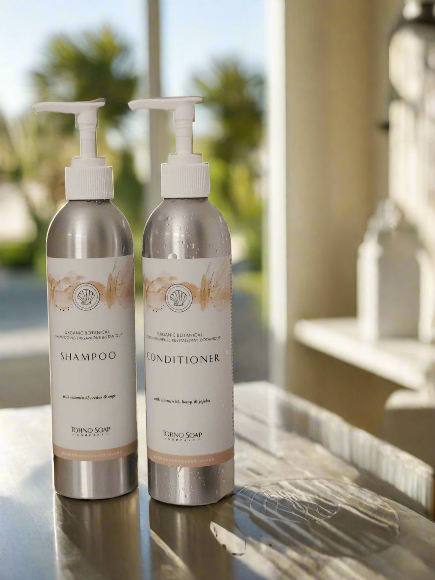 Two bottles of shampoo and conditioner with a loofah and gloves on a bathroom counter.