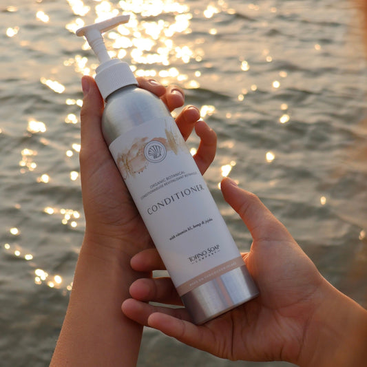 Person holding a bottle of conditionerby a body of water at sunset