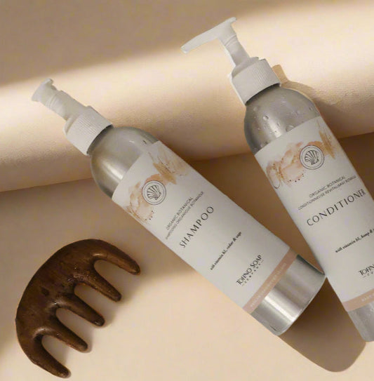 Two bottles of shampoo and conditioner with a wooden comb on a beige background