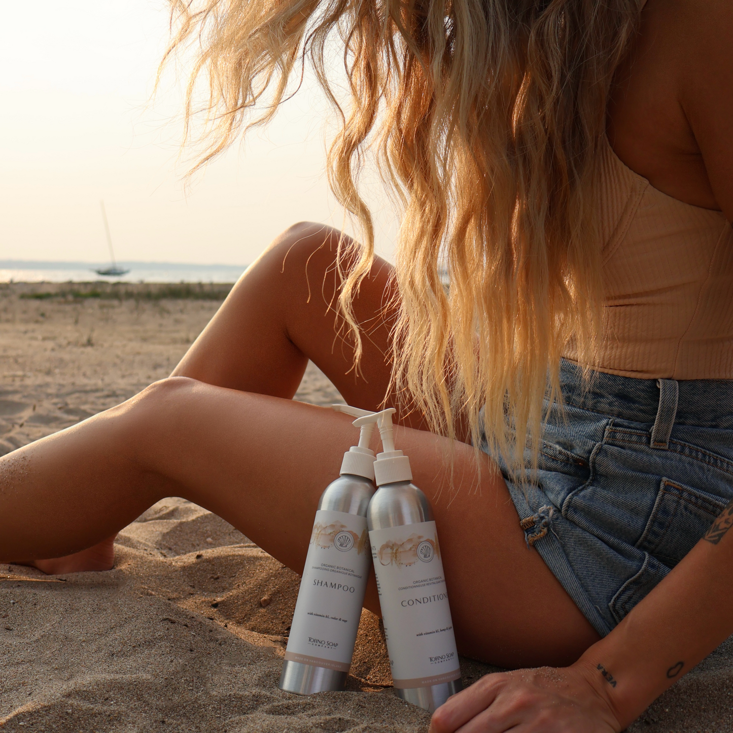 Person sitting on sand with two bottles of haircare
