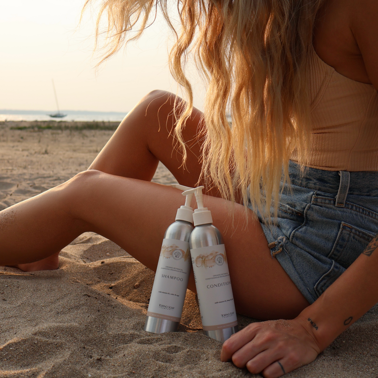 Person sitting on sand with two bottles of hair products