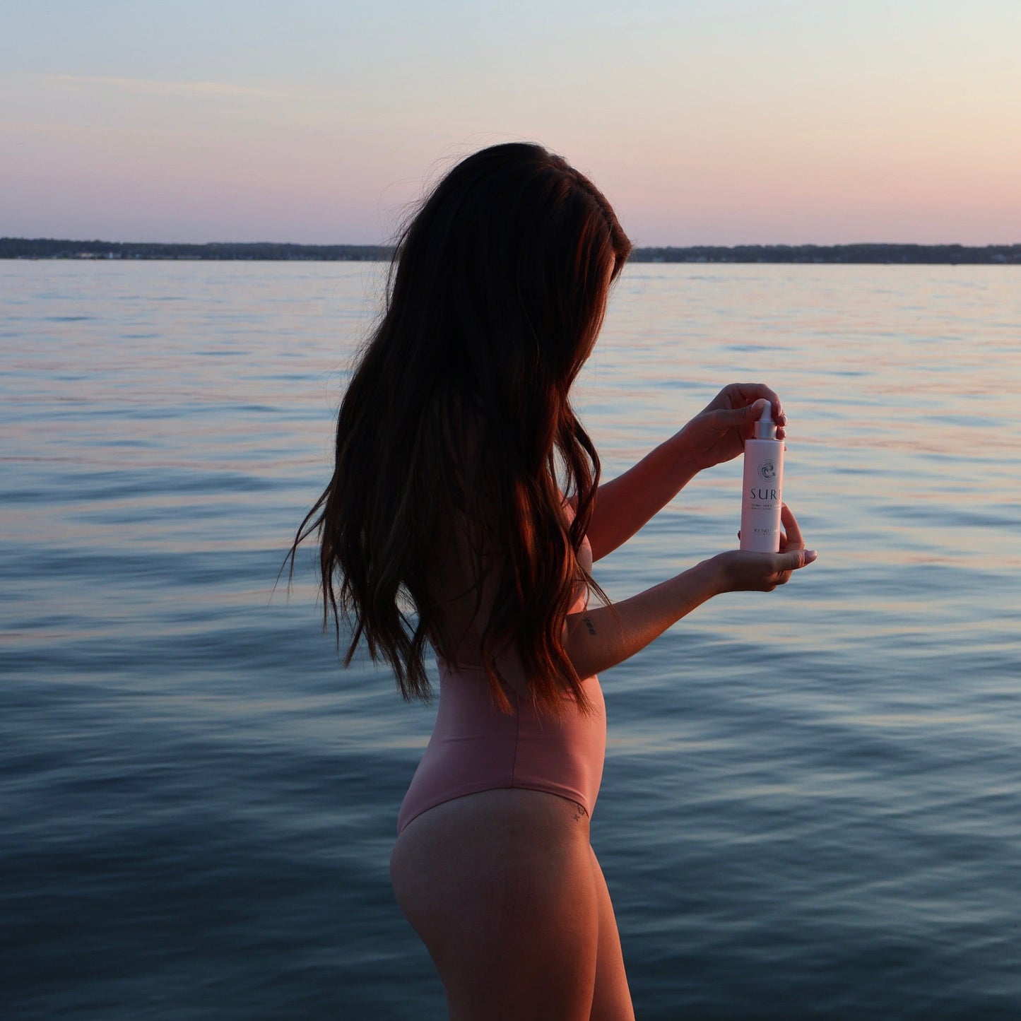 Woman holding a bottle by a lake at sunset