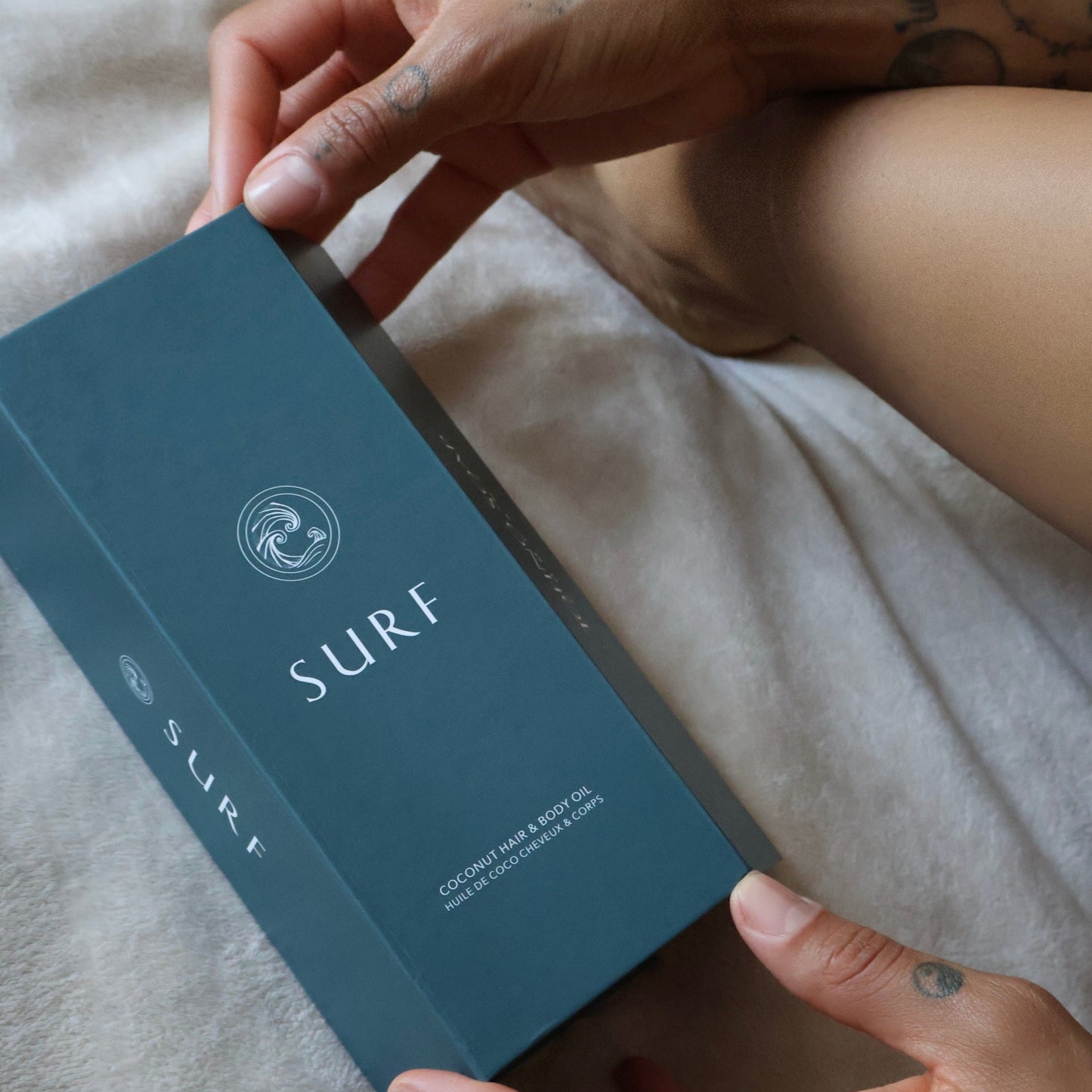 Person holding a 'SURF' product box on a bed