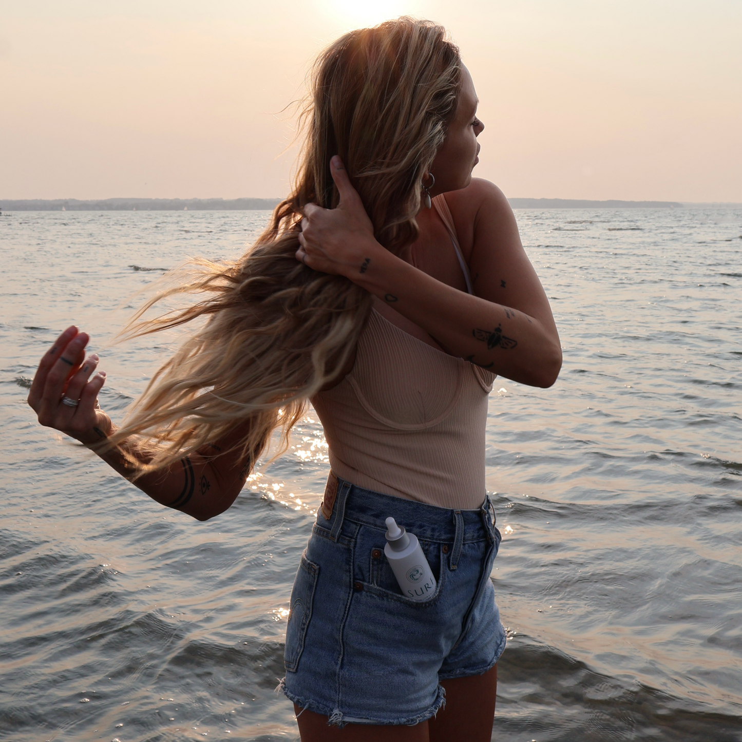 Woman standing on a beach at sunset, holding her hair.