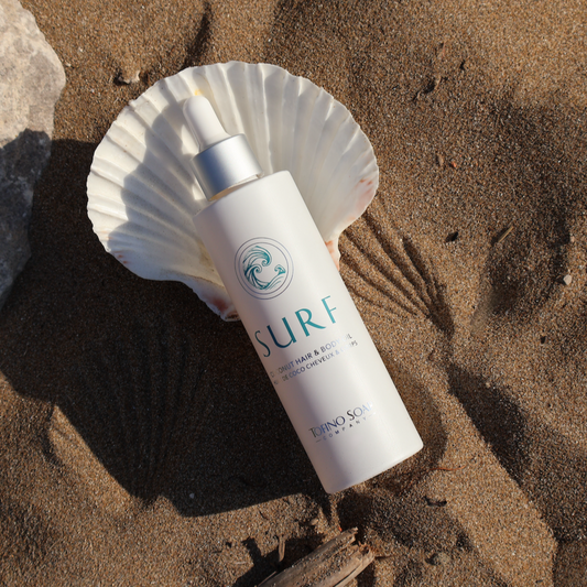 Skincare bottle labeled 'SURF' on a sandy surface with a shell nearby
