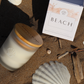 Candle, box labeled 'Beach', and seashell on sand