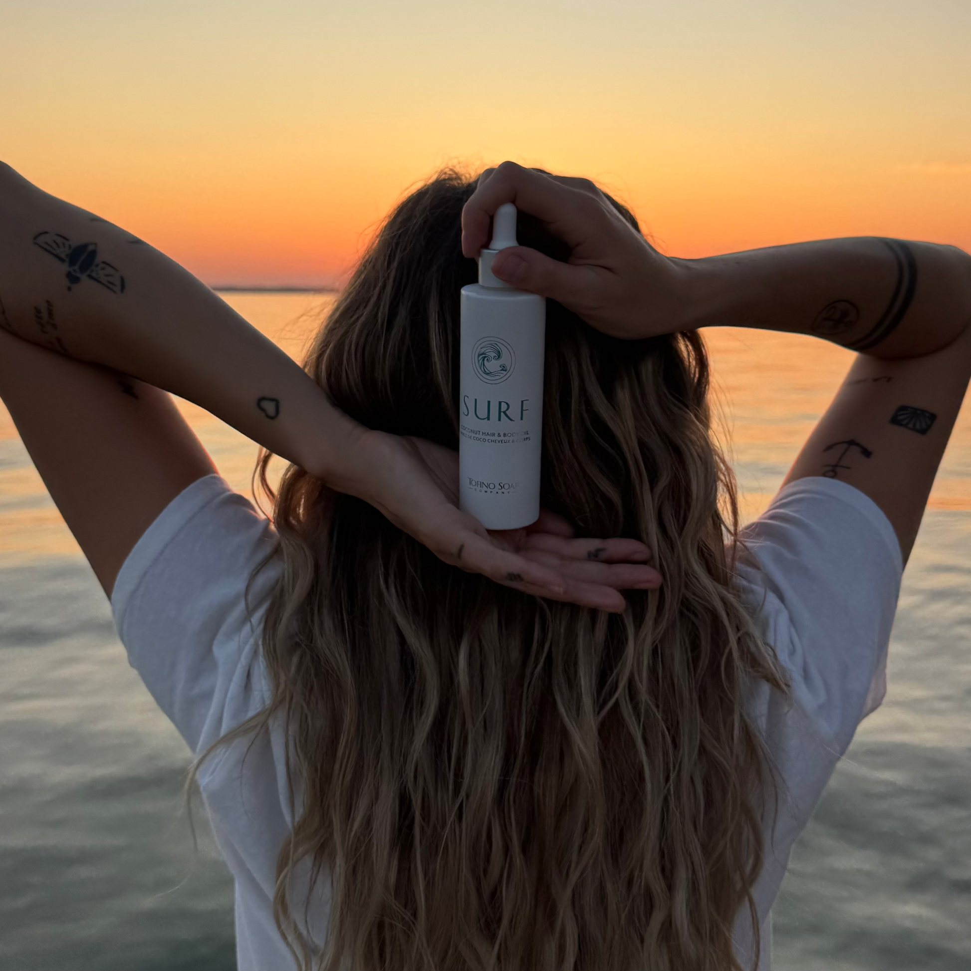 Person holding a bottle of SURF hair product with a sunset over water in the background
