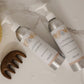 Two bottles of shampoo and conditioner with a scrubber and comb on a marble surface