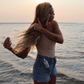 Woman standing on a beach at sunset, holding her hair.