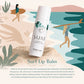 A white cylindrical lip balm bottle labeled SURF by Tropicaleaf Cosmetics, set against a stylized beach illustration with surfers, palm leaves, and teal water. Text below reads 'Surf Lip Balm' with a descriptive marketing paragraph.
