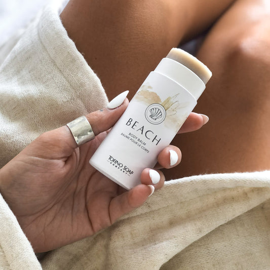 A person holding a stick of Beach Body Balm, with the product name and beach-themed packaging visible.